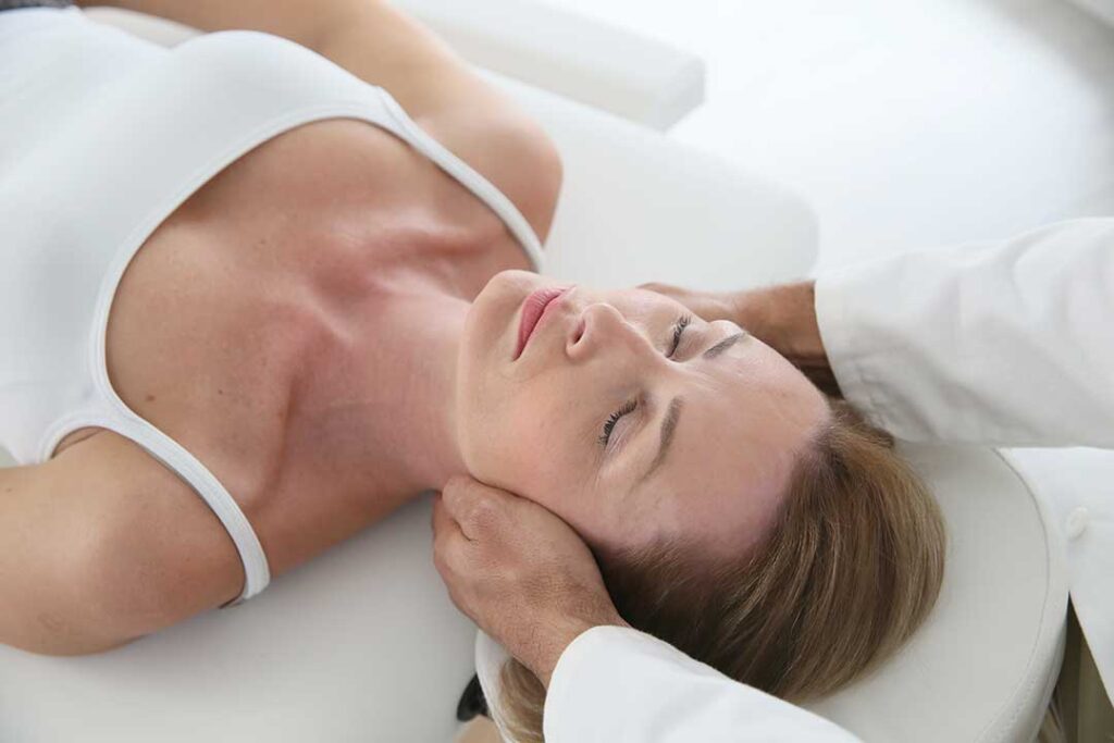 A person gently stretching their back and shoulders in a sunlit living room.
