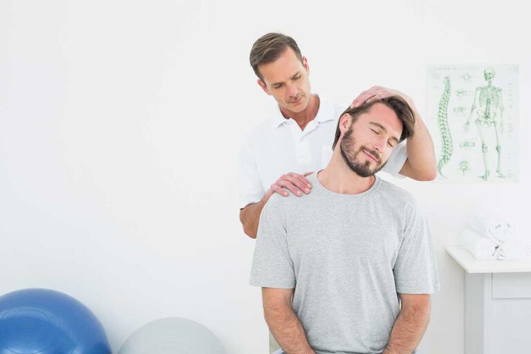 Person gently touching a sore jaw while seated at a desk with relaxed shoulders and a straight neck.